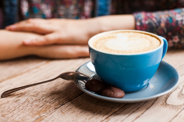 Galletas y taza de café con leche frente a la mujer sentada en la cafetería