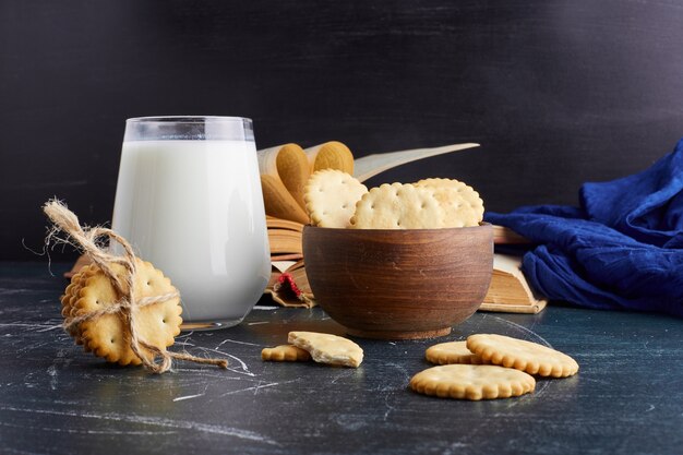 Galletas en una taza de madera con un vaso de leche.