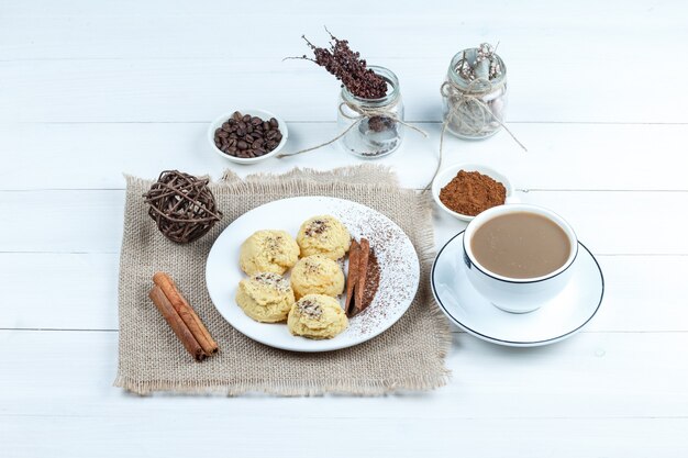 Galletas de vista de ángulo alto, canela, cuerdas en un pedazo de saco con un tazón de café instantáneo, una taza de café sobre fondo de tablero de madera blanca. horizontal