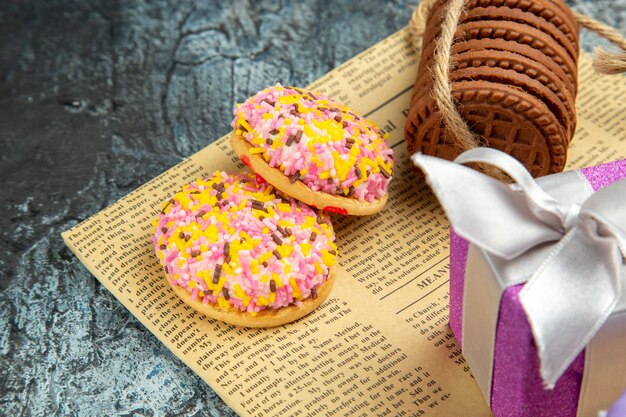 Galletas de vista frontal atadas con cuerdas regalo de navidad coloridas galletas de malvavisco en periódico sobre fondo gris