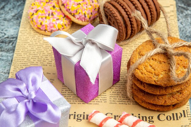 Galletas de vista frontal atadas con cuerdas regalos de navidad coloridas galletas de malvavisco en periódico sobre fondo gris