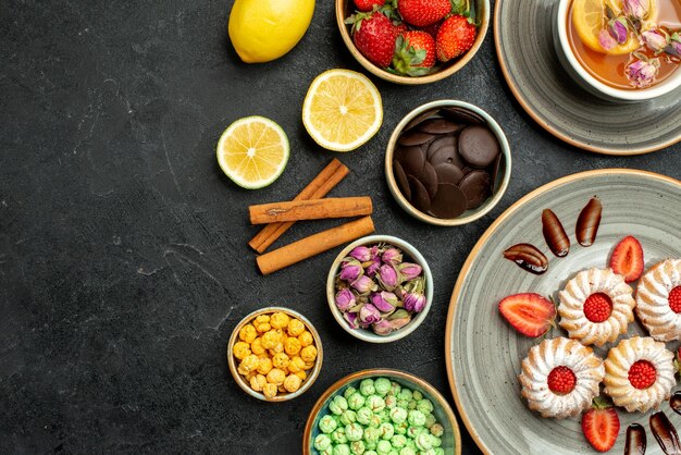 Galletas de vista superior de primer plano con galletas de té con té negro de fresa con tazones de limón de chocolate y diferentes dulces en el lado derecho de la mesa