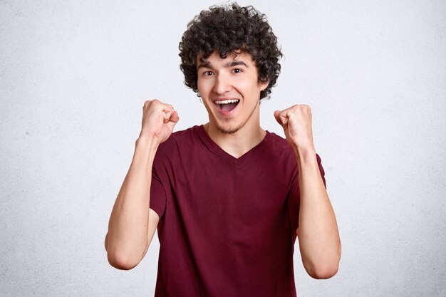 Ganador masculino con cabello rizado, aprieta los puños y exclama con felicidad