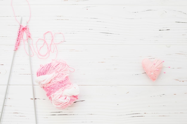 Ganchillo e hilado cerca de alfileres de costura en cojín rosa en forma de corazón