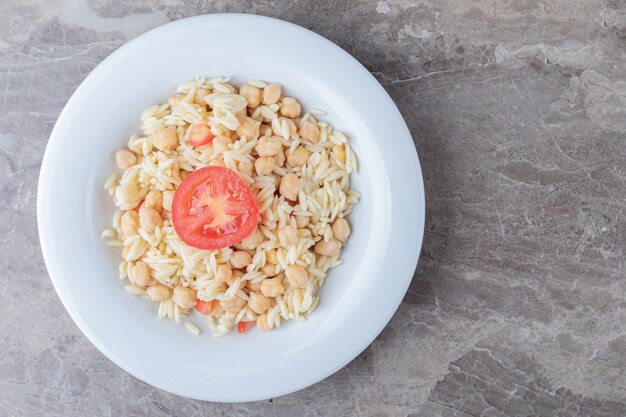 Garbanzos y pasta con rodajas de tomate en el plato, sobre el mármol.