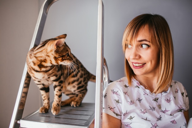 Gato de Bengala se encuentra en la escalera detrás de una mujer bonita