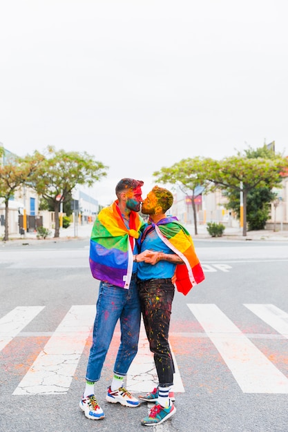 Gays con bandera de arcoiris besándose en la calle
