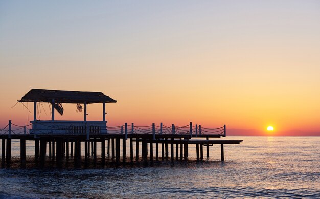 Gazebo en el muelle de madera en el mar con el sol al atardecer.