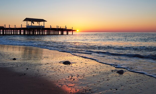 Gazebo en el muelle de madera en el mar con el sol al atardecer.