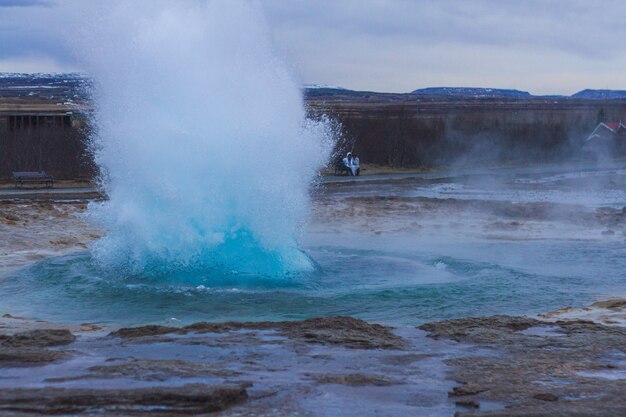 Géiser Strokkur rodeado por colinas bajo un cielo nublado en la noche en Islandia