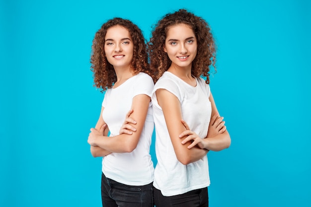 Foto gratuita gemelos de mujer posando con los brazos cruzados, sonriendo sobre azul.