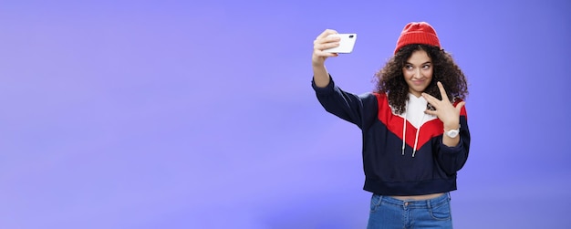 Foto gratuita genial y elegante mujer caucásica de buen aspecto con cabello rizado en un moderno gorro rojo y sudadera lo