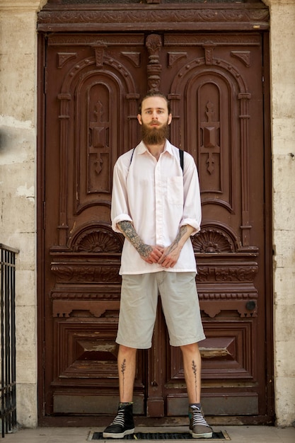 Genial hipster con camisa blanca posando frente a una puerta. Estilo y diversidad