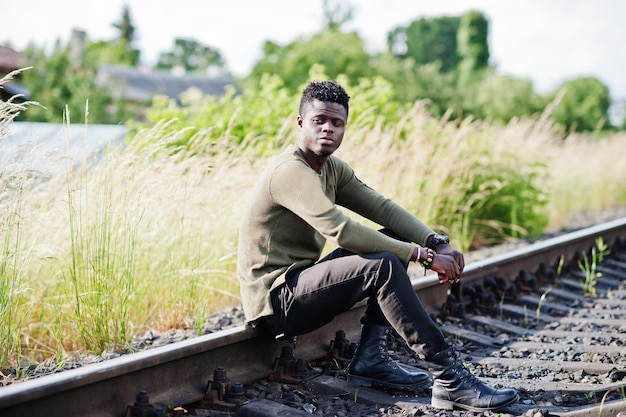 Genial hombre afroamericano negro sentado y posando en el ferrocarril en el campo