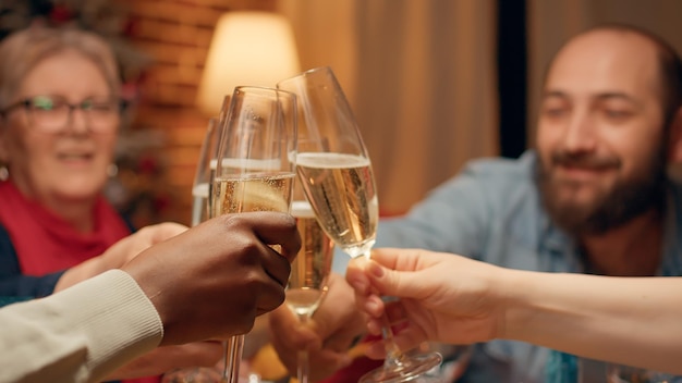 Gente alegre reunida en la mesa de la cena de Navidad para celebrar las vacaciones de invierno en la sala de estar. Felices y sonrientes miembros de la familia celebrando las tradicionales vacaciones de invierno en casa con vino espumoso.