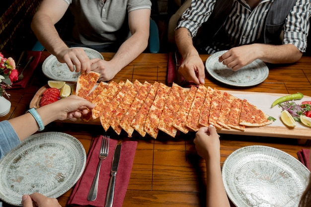 La gente alrededor de la mesa takind lahmacun rebanadas.