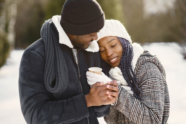 La gente camina afuera. Día de invierno. Pareja africana con café.