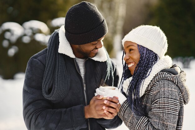 La gente camina afuera. Día de invierno. Pareja africana con café.