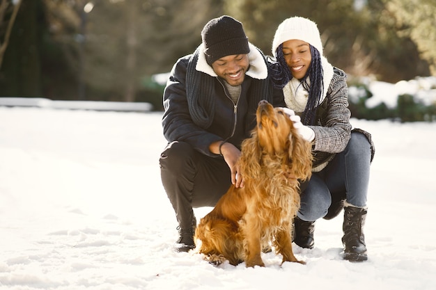 La gente camina afuera. Día de invierno. Pareja africana con perro.