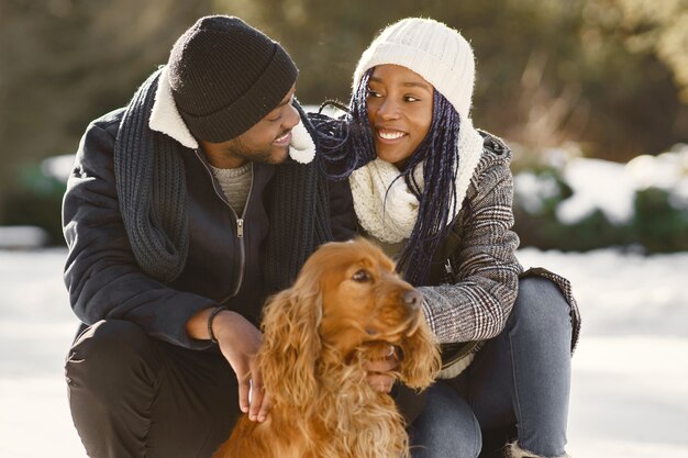 La gente camina afuera. Día de invierno. Pareja africana con perro.