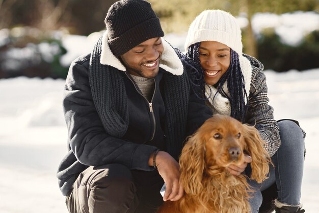 La gente camina afuera. Día de invierno. Pareja africana con perro.