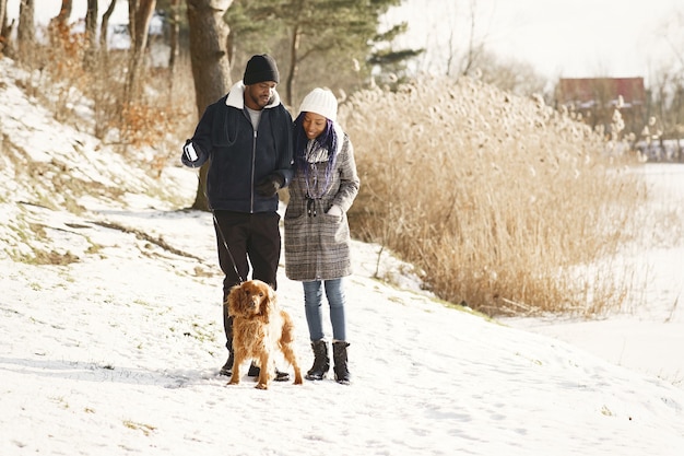 La gente camina afuera. Día de invierno. Pareja africana con perro.