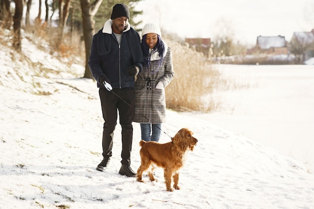 La gente camina afuera. Día de invierno. Pareja africana con perro.