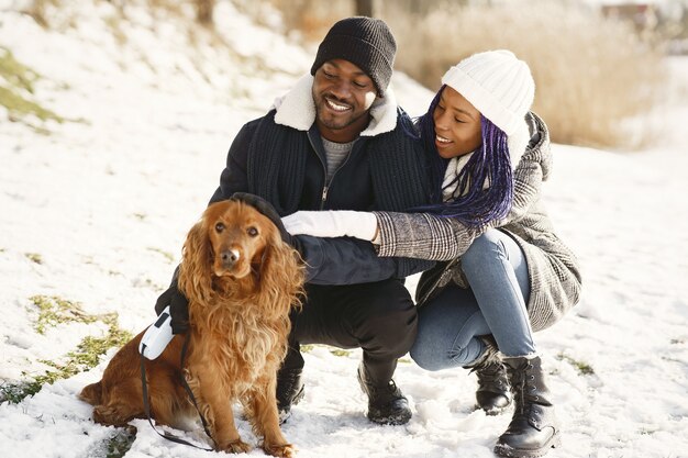 La gente camina afuera. Día de invierno. Pareja africana con perro.