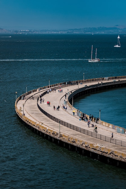 Gente caminando sobre un puente de hormigón sobre el mar azul durante el día