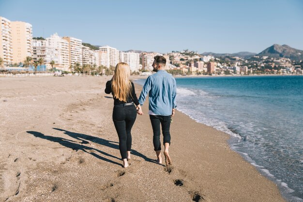 Gente cariñosa caminando en la playa cogidos de la mano