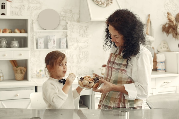 Gente en una cocina. Abuela con hija pequeña. Mujer adulta dar galletas de niña.