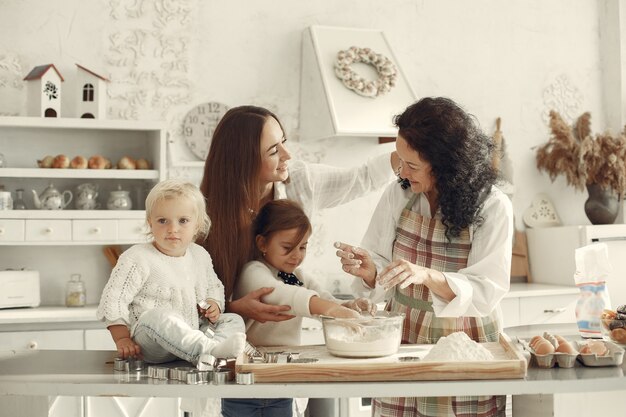 Gente en una cocina. Familia prepara pastel. Mujer adulta con hija y nietos.