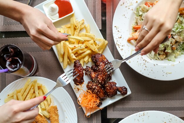 Gente comiendo alitas de pollo con salsa barbacoa y papas fritas