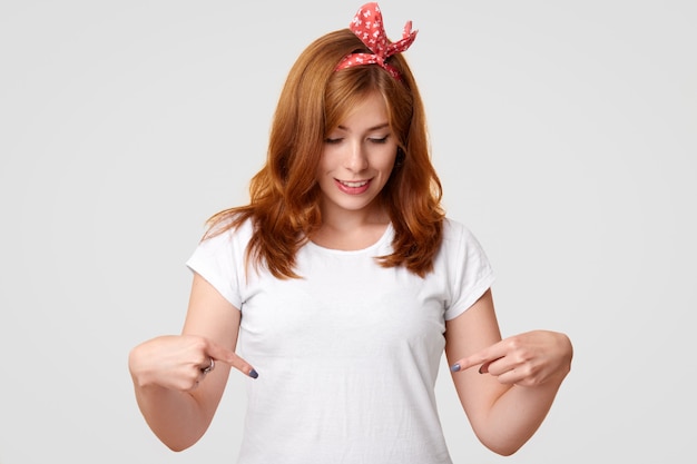 Gente, estilo, publicidad, concepto de ropa. Encantadoras puntos femeninos encantadores en la camiseta blanca con espacio de copia para su logotipo o promoción, se alegra de la nueva compra, aislada en blanco