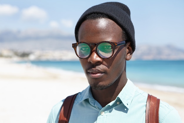 Gente, estilo de vida, verano y viajes. Retrato al aire libre de hipster atractivo relajante solo en la playa, disfrutando de un clima cálido y soleado