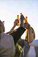 Foto gratuita gente feliz animando con botellas de cerveza contra la puesta de sol. relajado jóvenes amigos relajarse juntos en el parque. concepto de ocio