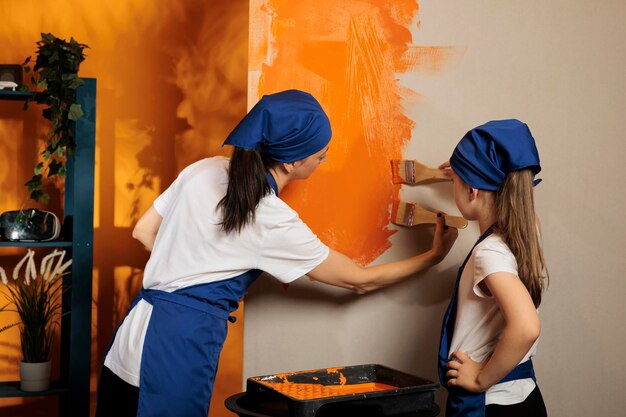 Gente feliz pintando paredes con pincel, divirtiéndose con el trabajo de renovación de bricolaje en el apartamento. Usando pintura de color naranja para redecorar la habitación, trabajando en la mejora de la casa con herramientas de pincel.