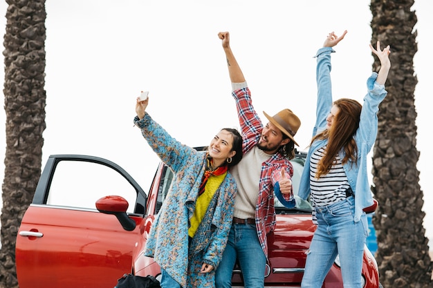 Gente feliz tomando selfie cerca de coche rojo en la calle