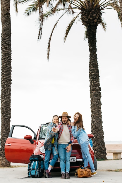 Gente feliz tomando selfie cerca de coche rojo