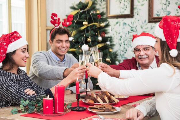Gente haciendo copas de champán en la mesa navideña