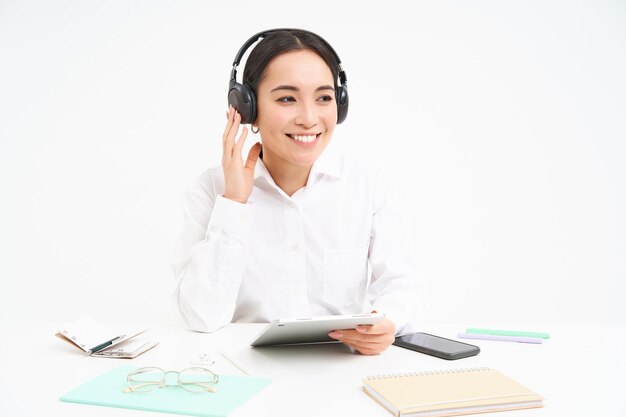 La gente y el lugar de trabajo mujer asiática sonriente se sienta en la oficina estudiante escuchando música en auriculares y ho