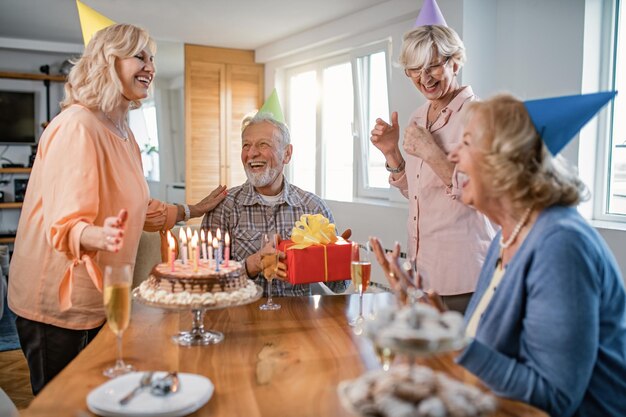 Gente madura feliz divirtiéndose mientras celebra su cumpleaños en casa El foco está en el hombre con un regalo de cumpleaños