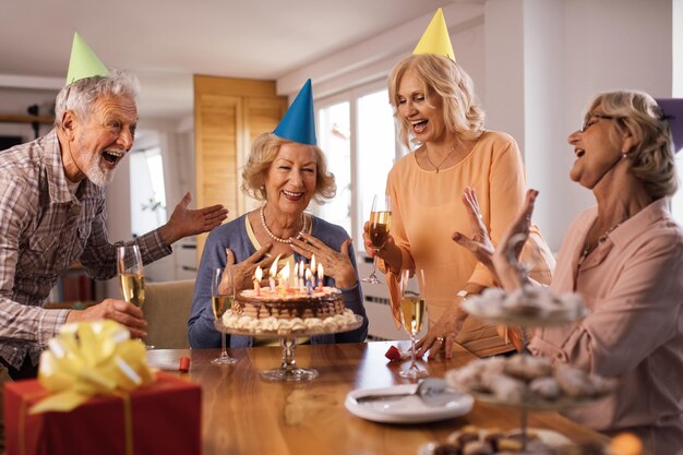 Gente madura feliz firmando mientras sorprende a sus amigos en pastel de cumpleaños en casa