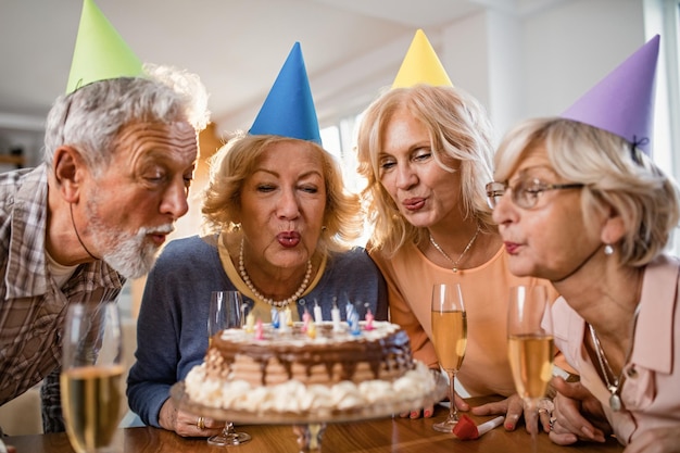 Gente madura feliz soplando velas de cumpleaños en un pastel y divirtiéndose en la fiesta de casa
