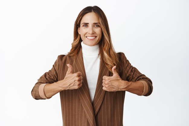 Gente de negocios Sonriente mujer corporativa que muestra los pulgares hacia arriba y parece complacida dar permiso cumplido fondo blanco de buena calidad