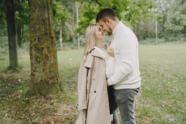 Gente en un parque. Mujer con un abrigo marrón. Hombre con un suéter blanco.