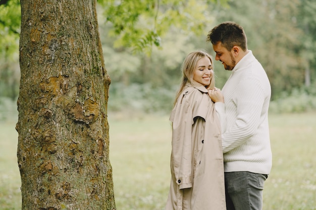 Gente en un parque. Mujer con un abrigo marrón. Hombre con un suéter blanco.