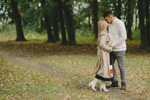 Gente en un parque. Mujer con un abrigo marrón. Hombre con un suéter blanco.