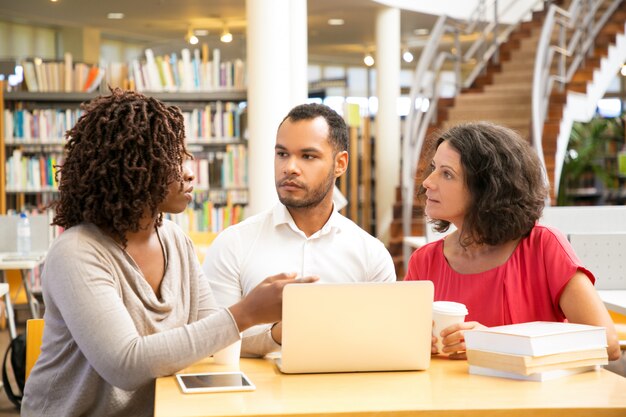 Gente pensativa hablando mientras usa la computadora portátil en la biblioteca