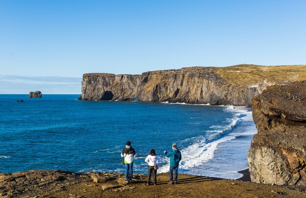 Gente de pie en la orilla rodeada por el mar con el Dyrholaey en Islandia